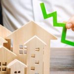 Analyst holds down arrow near the wooden houses. Concept of falling real estate market. Low prices and cost of housing. Reduced mortgage rates and housing demand. Bankruptcy. Crisis and low liquidity