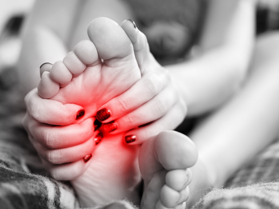 Black and white photo of a woman's hands with lacquered nails gripping her foot in pain. The pain area is signified with the colour red. | Photo by Viatris Malaysia/NHA File Photo