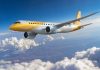 Scoot Embraer E190-E2 jet flying above the clouds that float over a city under a blue sky. | Photo by Scoot / NHA File Photo