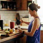 Happy sportswoman pouring herself fruit smoothie in the kitchen.